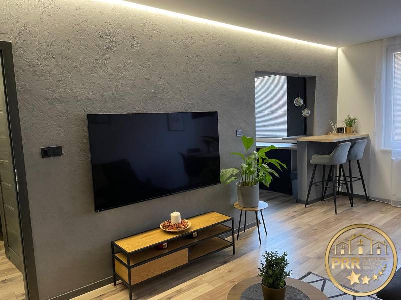 Living room in a 3-room apartment with a modern TV, plants, and a bar counter with high stools.