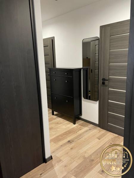 Hallway of a 3-room apartment with wooden flooring, a black dresser, and a mirror.