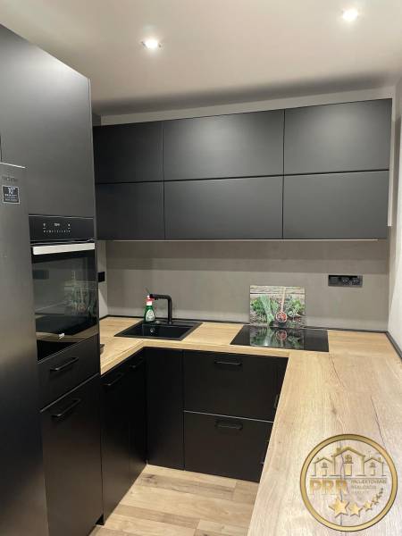 A kitchen in a 3-room apartment with black cabinets and a wooden countertop.