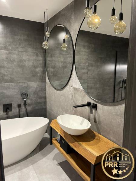A bathroom in a 3-room apartment with stylish mirrors, a bathtub, and a wooden washbasin counter.