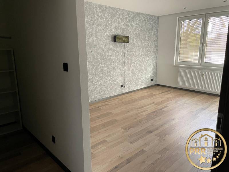Empty room in a 3-bedroom apartment with wooden flooring and a structural wall.