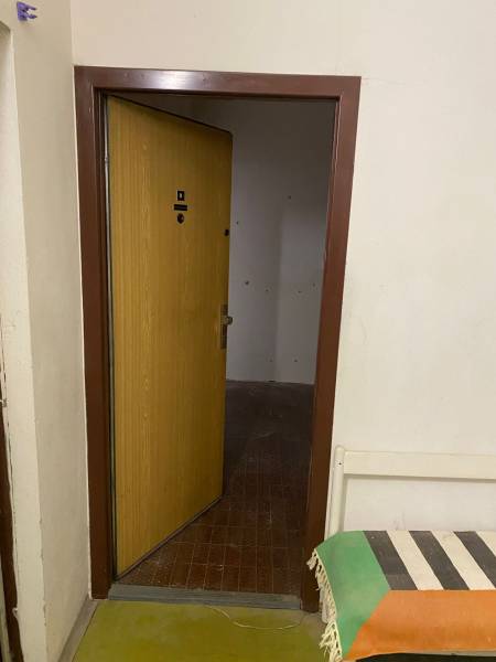 Open door in a 3-room apartment with a tiled floor and a bench with a colorful throw.