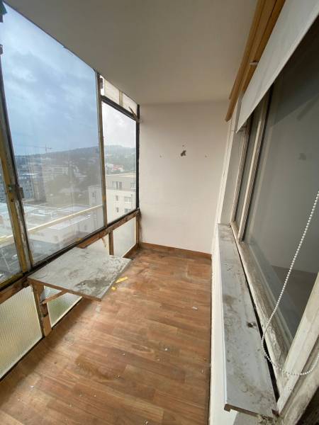 A glazed balcony of a 3-room apartment with a wooden floor and a view of the rooftops of buildings.