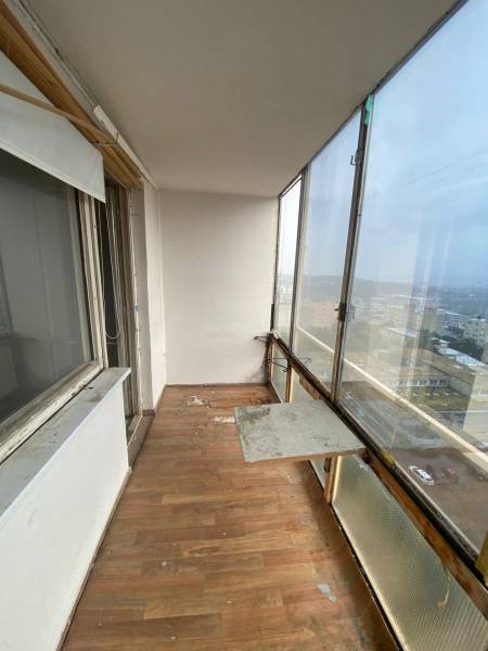 Glazed loggia with wooden flooring in a 3-room apartment, view of the exterior.