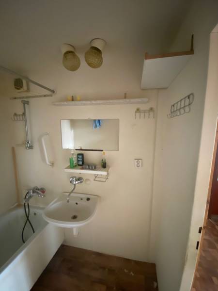 A bathroom with a bathtub and a sink in a 3-room apartment with storage shelves.