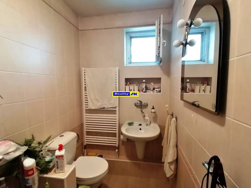 A bathroom in a family house with a sink, mirror, and shelves with light tiles.