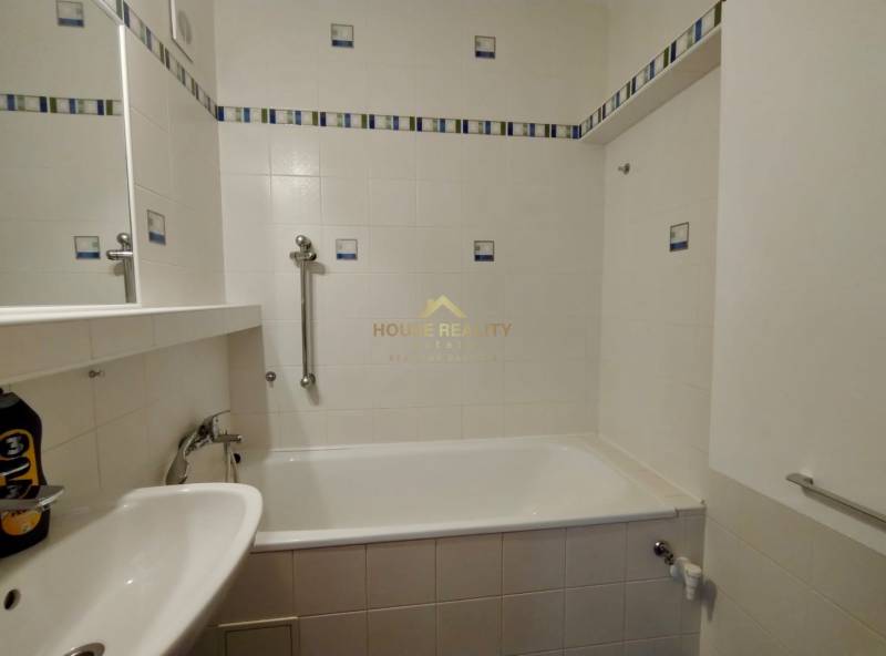 A bathroom with a bathtub, white tiles, and handrails in a 3-room apartment.