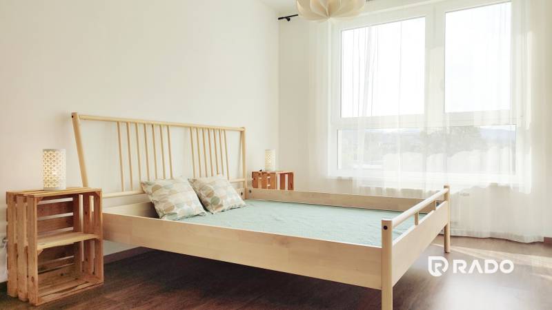 A bedroom with light wooden furniture and a large window in a 2-room apartment.