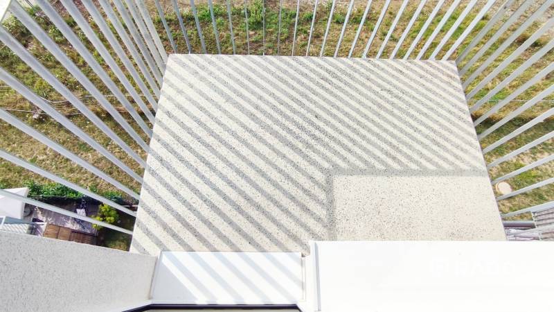 A balcony with a concrete floor and metal railing, facing the garden.