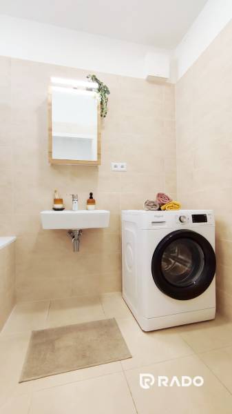 A bathroom in a 2-room apartment with a sink, a washing machine, and a towel rack.