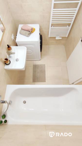 Bathroom with a bathtub, sink, washing machine, and ladder radiator in a 2-room apartment.