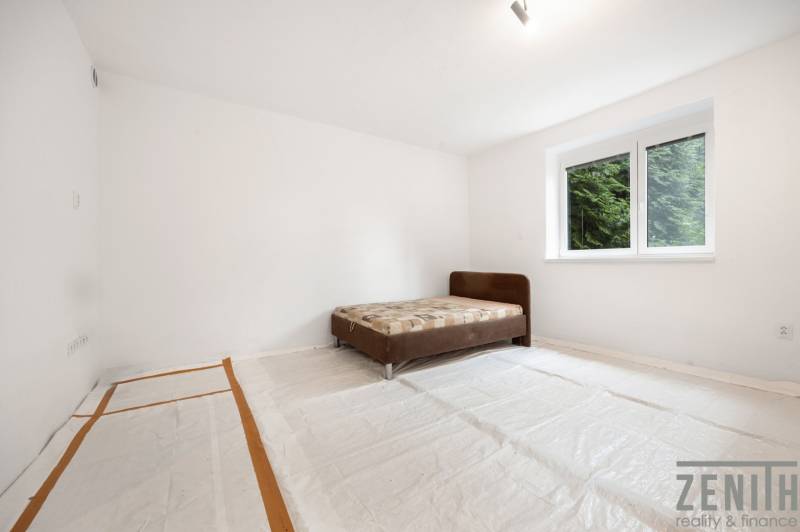 A room in a family house contains a bed and has a view of the forest through the window.