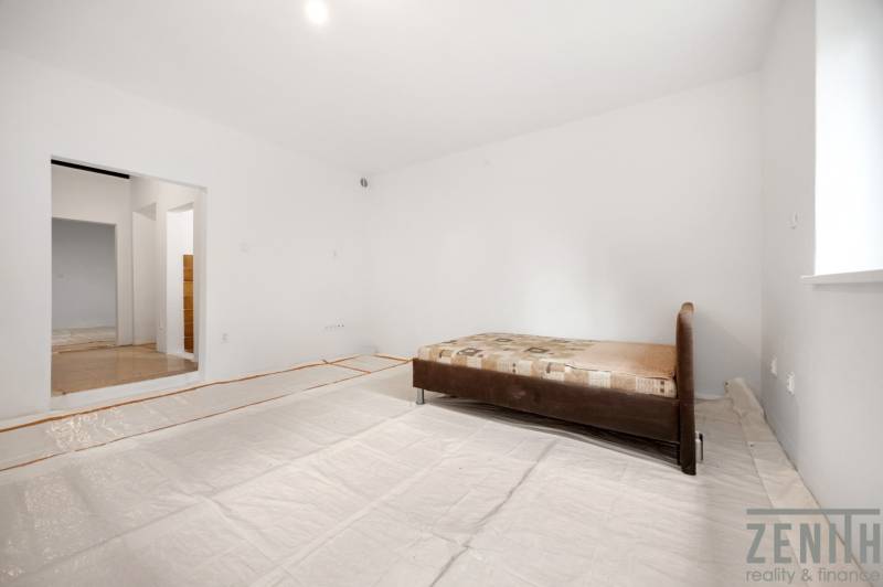 Bright room in a family house with a bed and an open passage to another part.