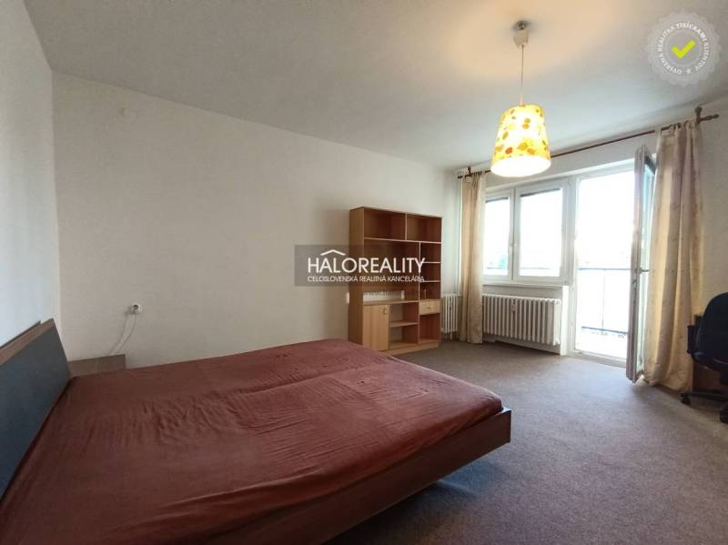 A bedroom in a studio apartment with a bed and a shelving unit, light curtains.