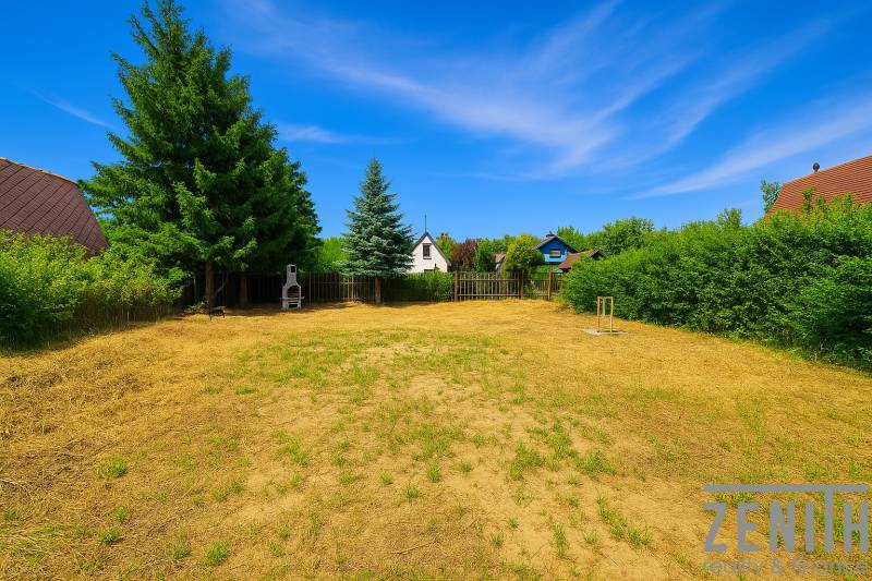 A spacious garden in Lozorno with a grill, bordered by tall trees and a wooden fence.