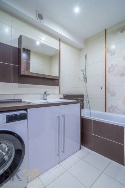A bathroom in a 3-room apartment with a shower, a washing machine, and a sink cabinet.