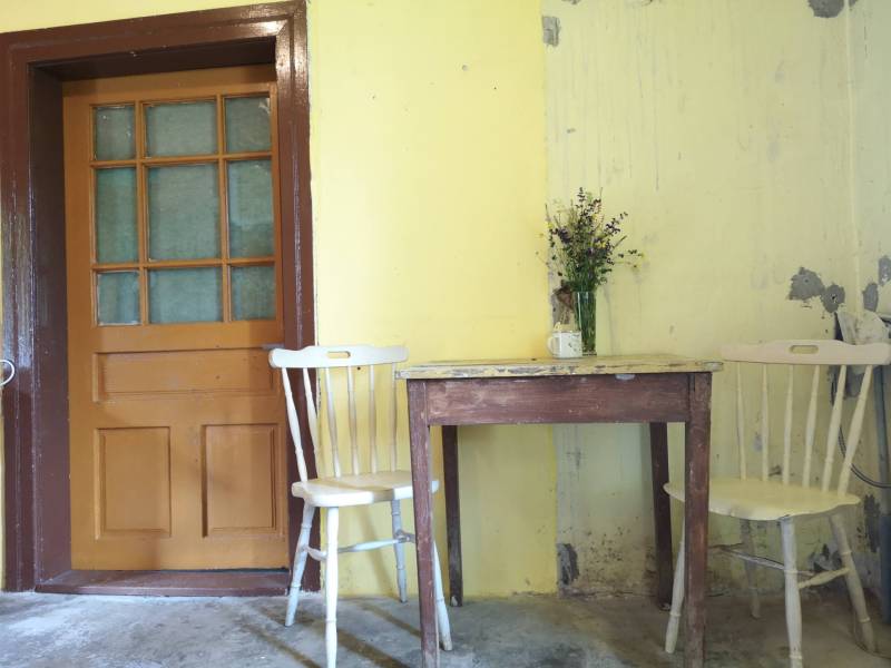 Yellow walls in a family house with a wooden table, chairs, and a small vase with flowers.