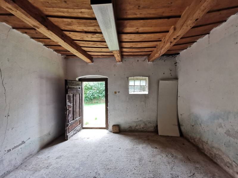 Interior of a family house with old wooden doors and ceiling beams, illuminated by a neon light.