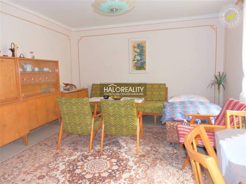 A room in a family house with wooden furniture, a carpet, and flowers in a decorative vase.