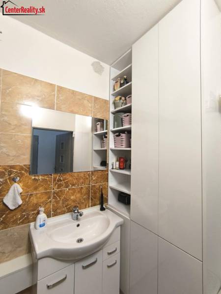 A bathroom in a 3-room apartment with a white sink, mirror, and storage cabinets.