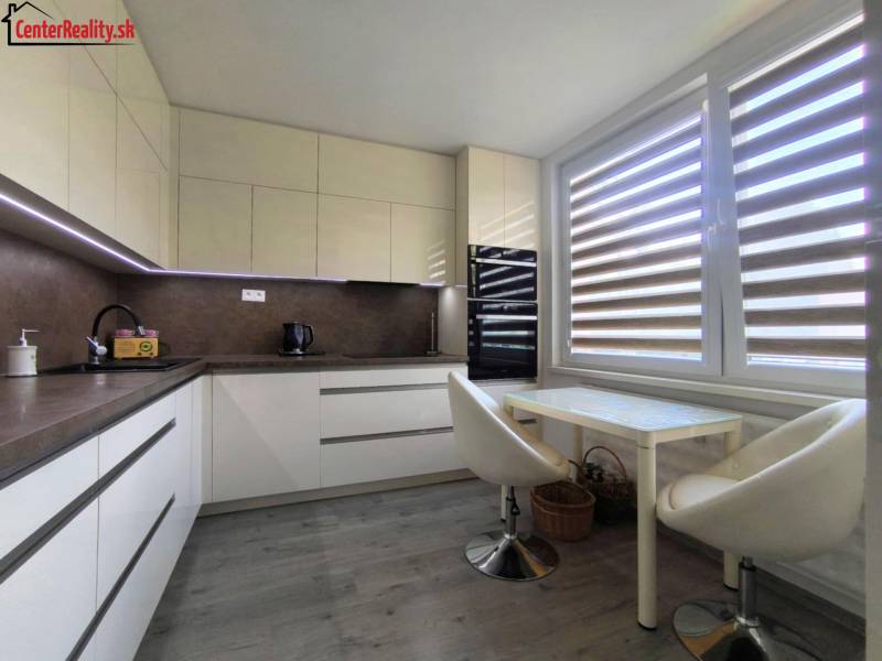 A kitchen in a 3-room apartment with seating and a large window with blinds.