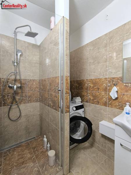 A bathroom with a shower and a washing machine in a 3-room apartment.
