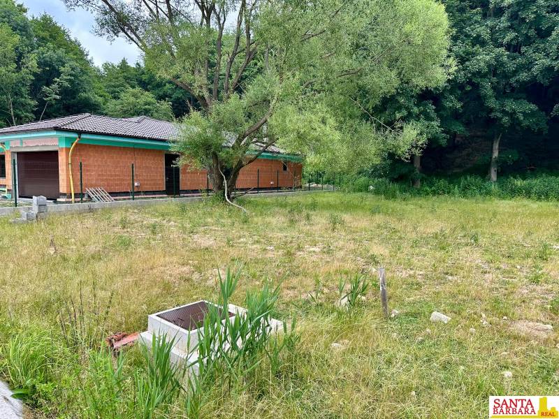 A plot for residential use in Borinka with trees and an unfinished house near the forest.