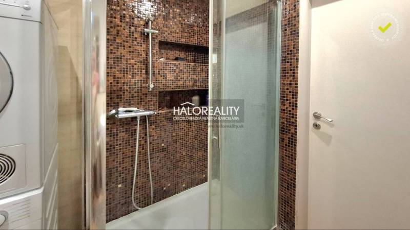 Bathroom with a washing machine, shower cabin, and mosaic tiles in a family house.