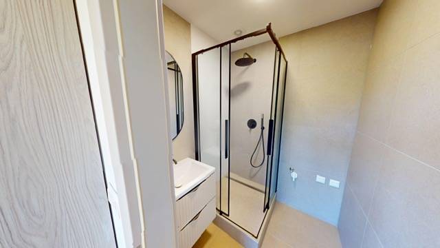 A bathroom in a 2-room apartment with a shower and a sink.