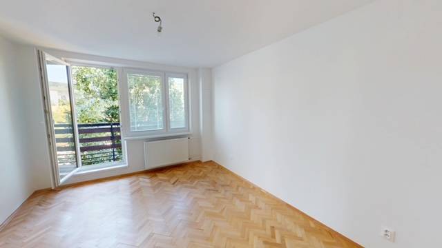 A spacious room in a 2-room apartment with wooden flooring and a large window to the balcony.