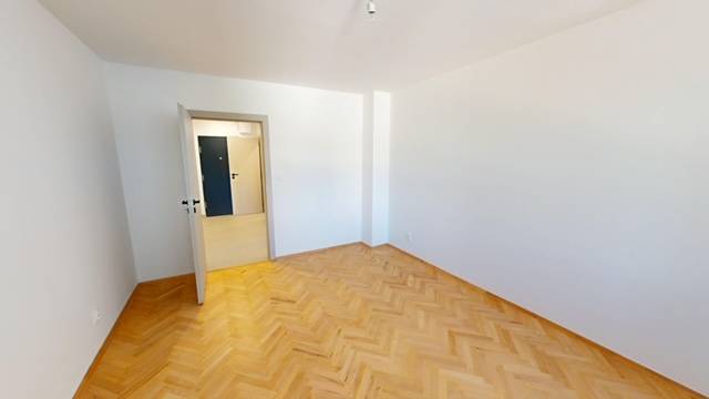 A room in a 2-room apartment with a parquet floor and white walls.
