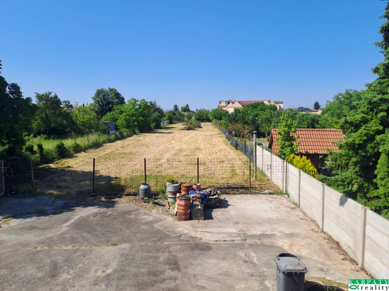 A reinforced area with greenery, barrels, and houses in Sládkovičovo, family houses in the background.