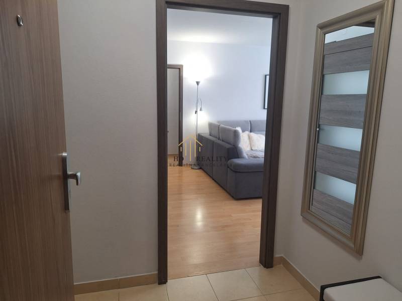 A hallway with a view of the living room in a 3-room apartment, visible couch and lamp.