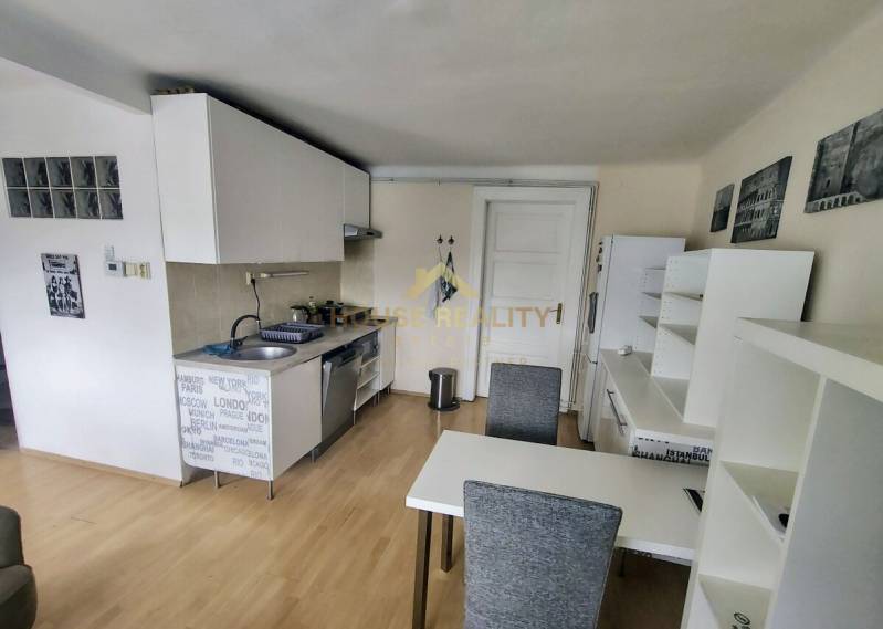 A kitchen in a 2-room apartment with a dining table, white cabinets, and wooden flooring.