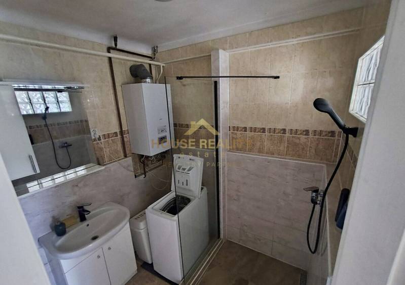 A bathroom in a 2-room apartment with a shower, washing machine, sink, and boiler.