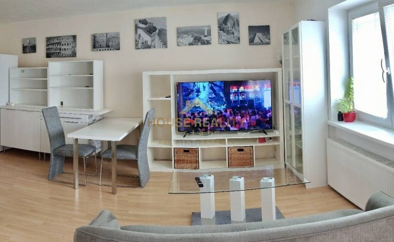 Living room in a two-room apartment with a TV, sofa, and dining table.