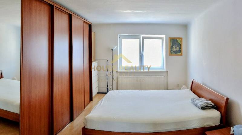 A bedroom with a wooden bed and wardrobe in a 2-room apartment, complemented by a window and a painting.