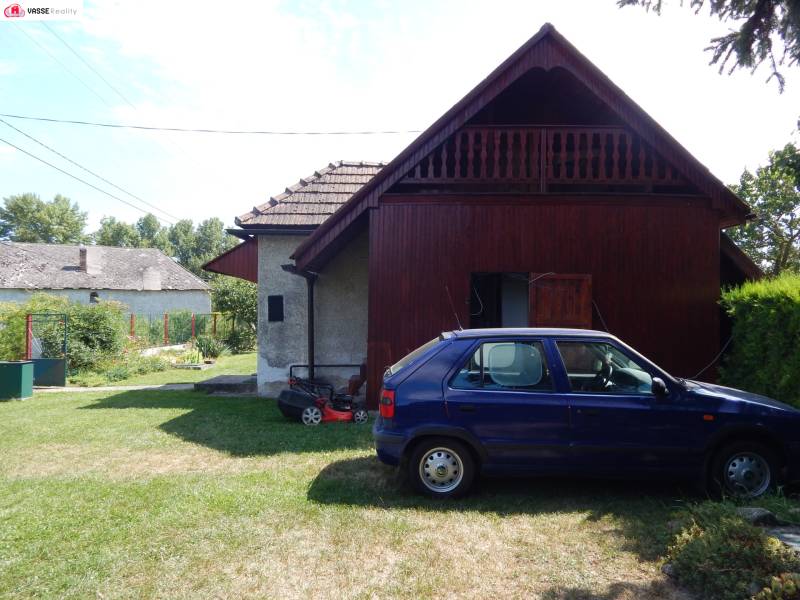 A car parked near the cottage in Klížska Nemá, surrounded by green lawn and trees.