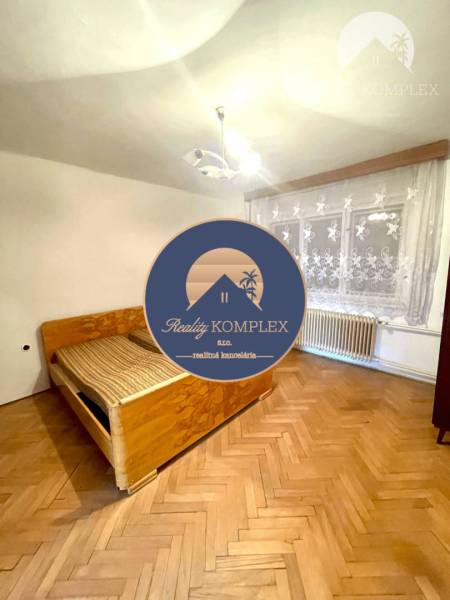 Interior of a family house with wooden flooring, a bed, and curtains on the window.