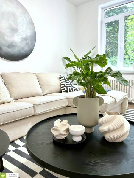 Bright living room corner with a sofa, a plant on a black table, geometric accessories.