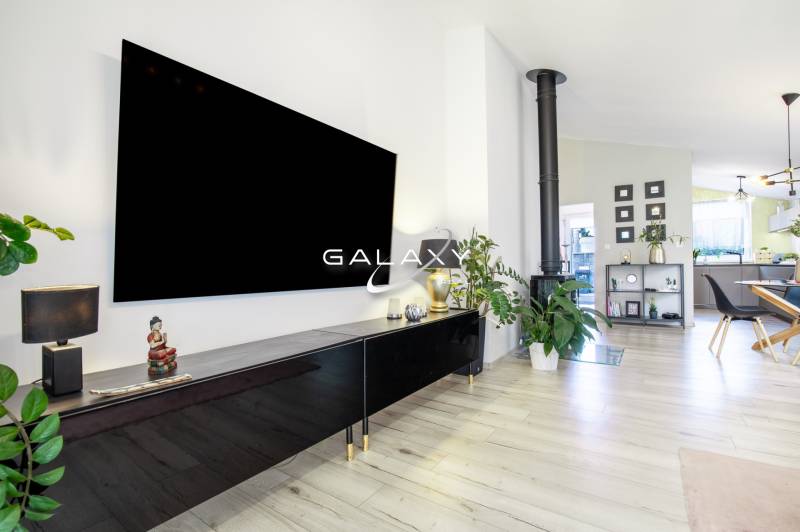 A modern living room interior in a family house with a fireplace, plants, and a large television.