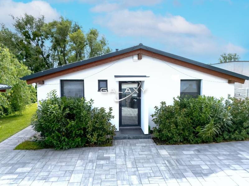 A family house in Čierna Voda with a white facade, surrounded by greenery and paving.