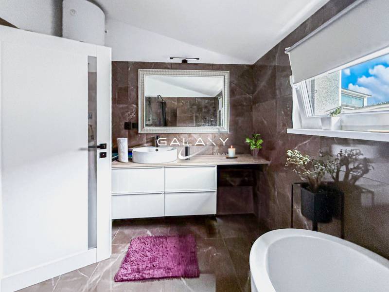 Bathroom in a family house with a bathtub, sink, and window, decorative plants.