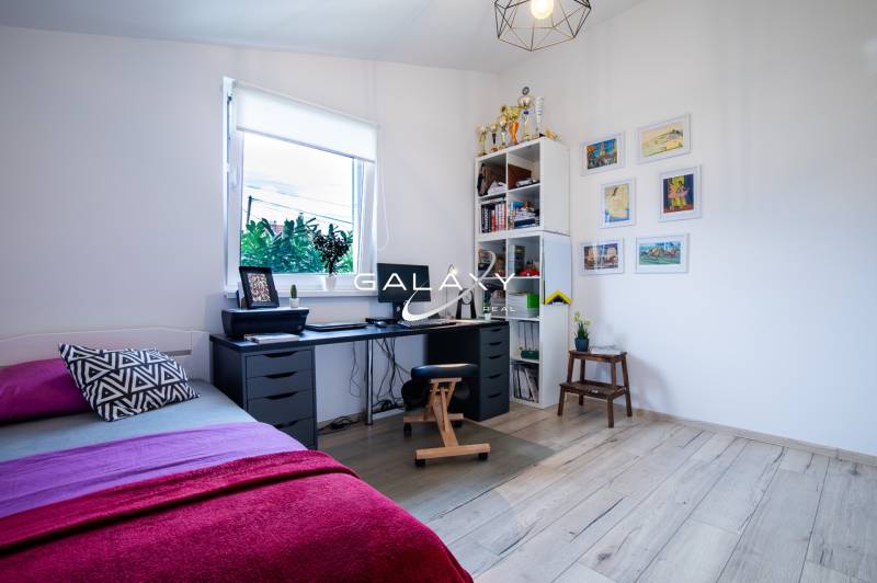 A workspace in a family house with a desk, bed, and a shelf with trophies.