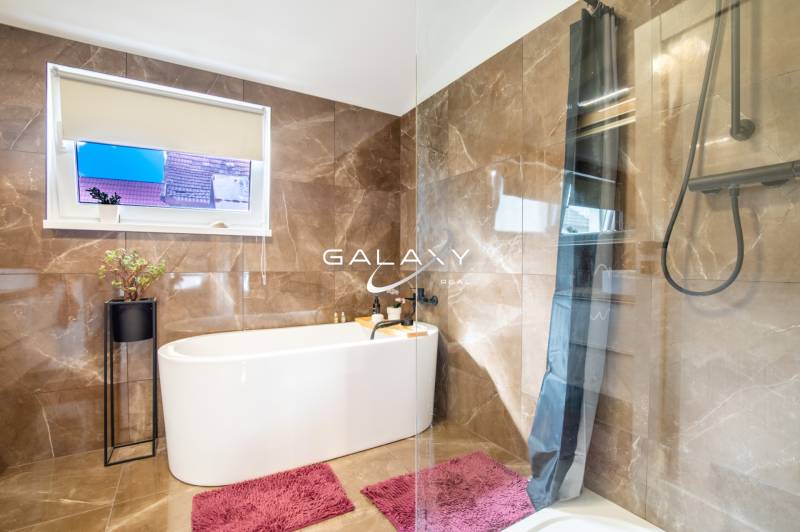 A bathroom in a family house with a bathtub, marble tiles, and pink carpets.