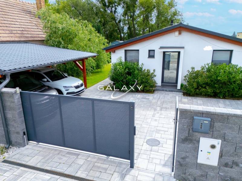 A family house in Čierna Voda with a car, a gate, and a landscaped garden.