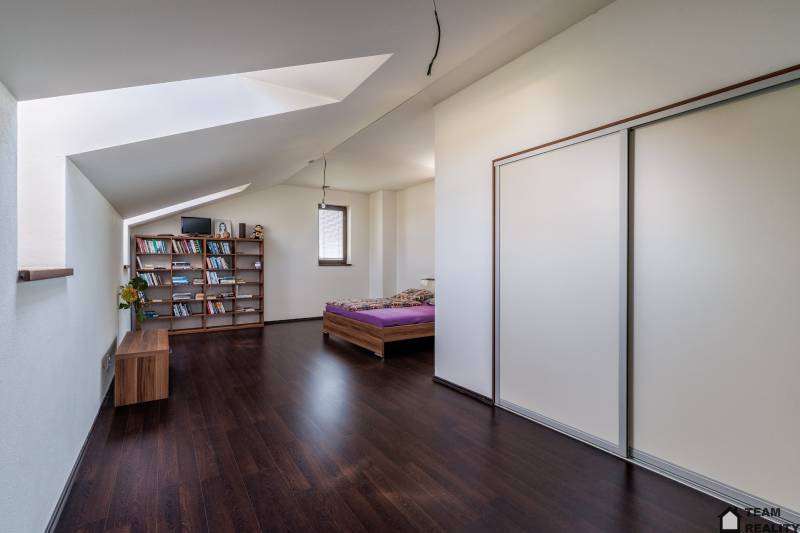 Attic bedroom with a bookshelf and a cabinet in a family house, dark floor.