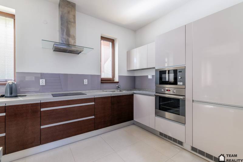 A kitchen in a family house with white and wooden cabinets and built-in appliances.