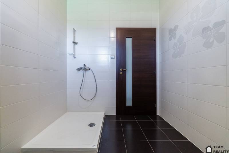 Shower enclosure with brown doors and a white tiled wall in a family house.