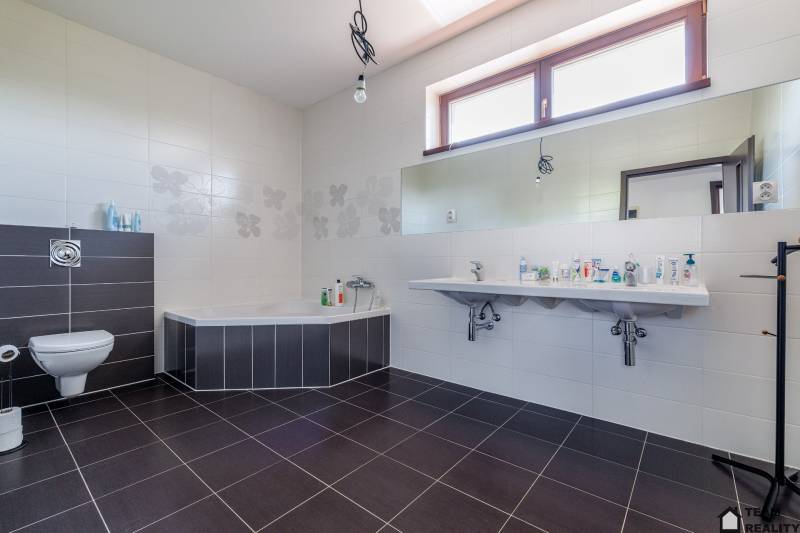 A bathroom in a family house with a bathtub, double sink, and toilet.